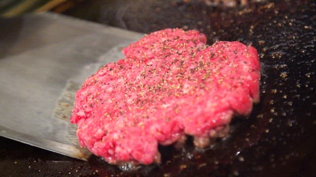 Seasoned beef patty cooking on a grill