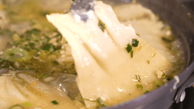 Tongs picking up dumpling soup boiling in broth