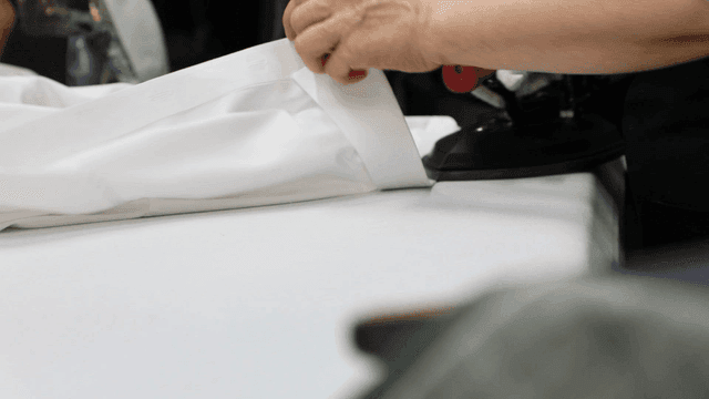 Hands ironing a white shirt on a table