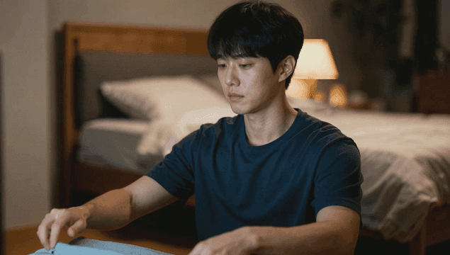 침실에서 모니터를 보며 옷을 개는 남자