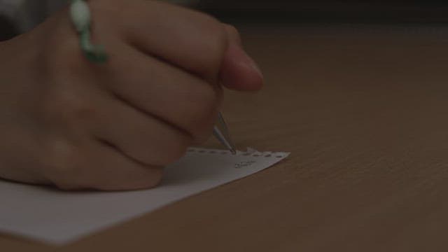 어두운 방에서 펜으로 작은 종이에 글씨를 쓰는 모습