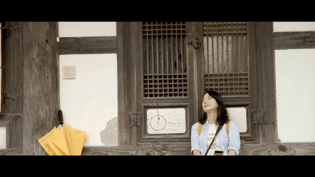 Woman wearing earphones resting while leaning against Hanok