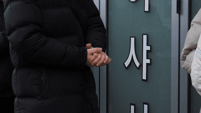 People standing outside building holding hand warmers while waiting