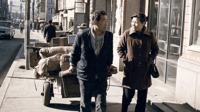 Man and woman walking and pulling cart on city street in 1970s