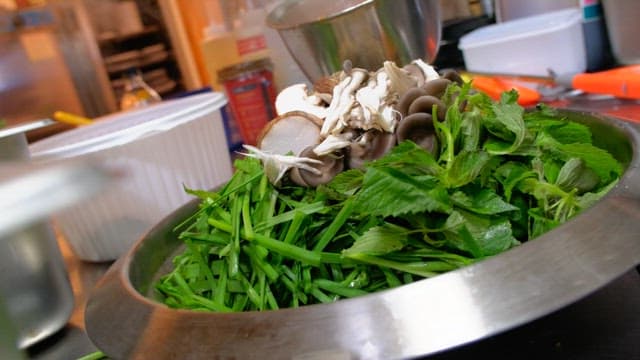 Hot pot dish made by pouring broth over fresh vegetables and mushrooms in a metal bowl