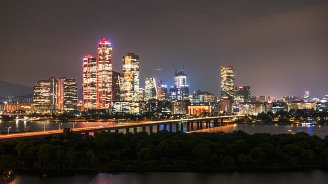 Night view of the brightly lit city skyline with a river flowing below bridge