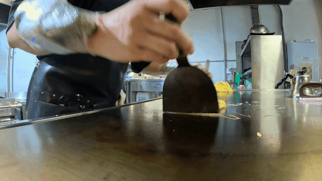 Skilled chef preparing egg omelet on griddle with stone-weighted arm