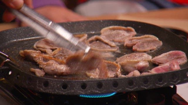 Grilling pork belly with tongs on the grill