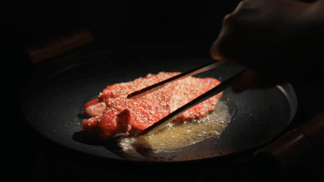 Steak sizzling in a pan with seasoning