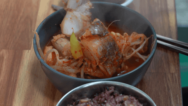Spoon scooping out steaming bowl of spicy fish stew