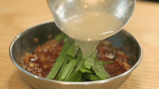 Broth poured over seasoning sauce containing chives and red pepper powder