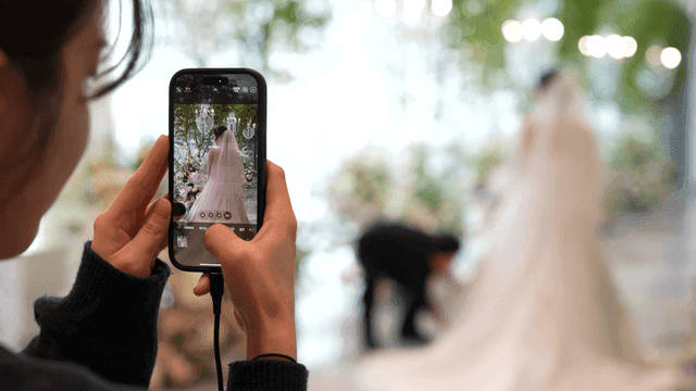 Woman taking picture of bride with her cell phone at wedding.