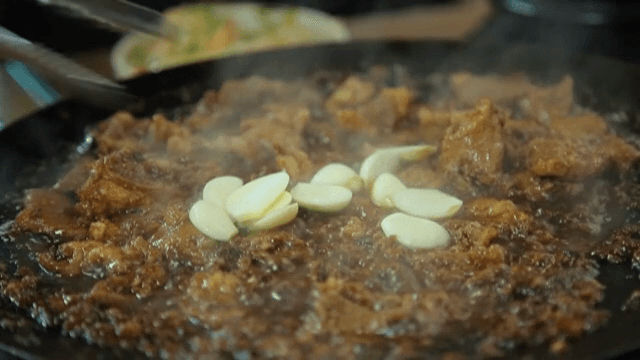 지글거리는 양념 갈비에 마늘을 추가하는 모습