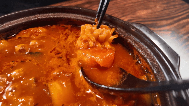 Chopsticks scooping seafood stew boiling in pot onto spoon