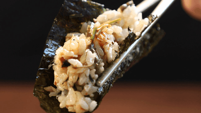Chopsticks holding rice wrapped in seaweed