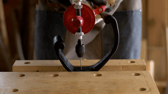 작업장에서 나무 조각을 수동 드릴로 가공하는 장인