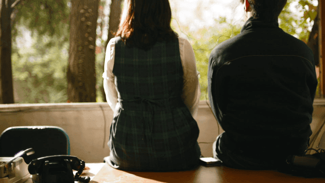 Back of couple sitting by window and listening to music together