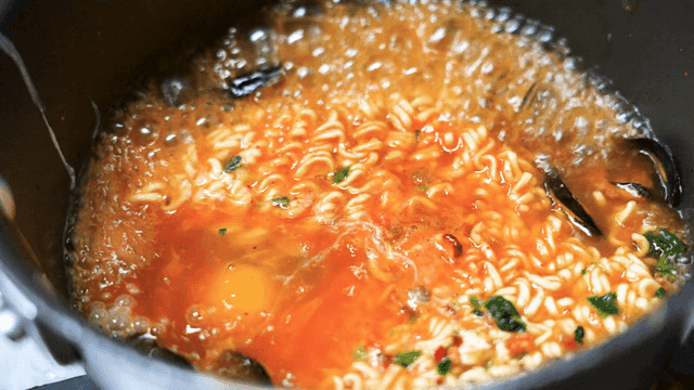 Raw egg added to mussel ramen boiling in pot