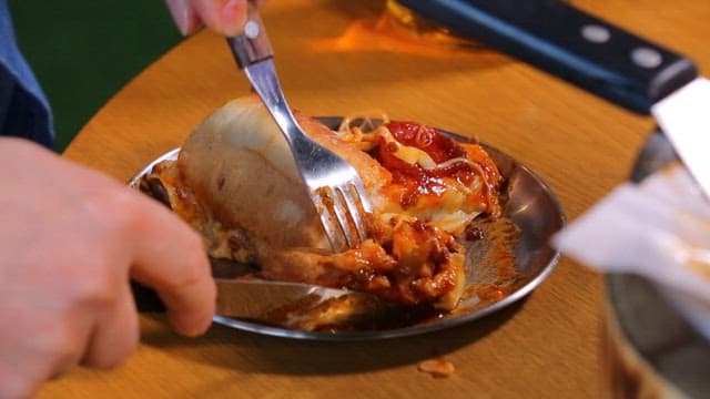 Slice of Chicago pizza with stretchy cheese being picked up with a fork and knife