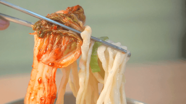 Chopsticks lifting kimchi and hand-cut noodles
