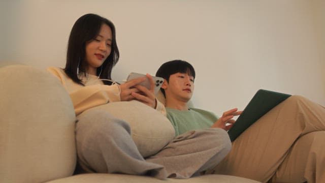 Two people using digital devices on a sofa in cozy living room