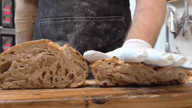 Baker pressing freshly baked campagne bread on wooden board
