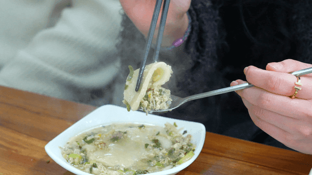 Woman putting hot dumpling soup onto spoon with chopsticks