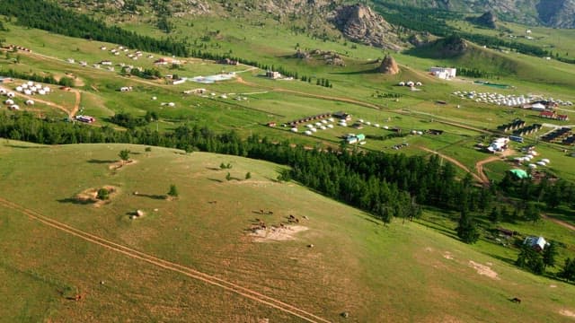 Vast green landscape with scattered yurts