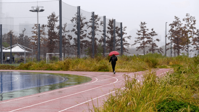 우산을 쓰고 비 오는 트랙을 걷는 사람