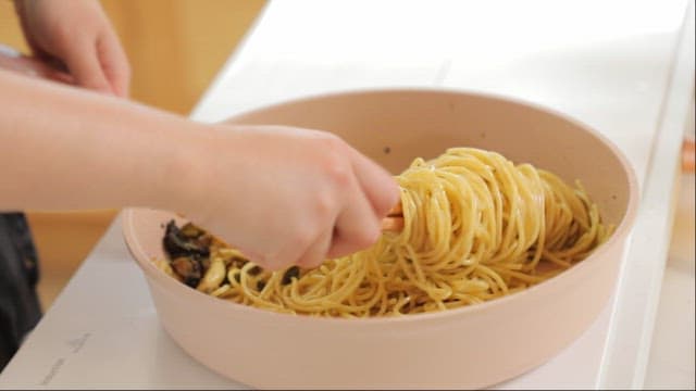 Person twirling pasta with chopsticks in a frying pan
