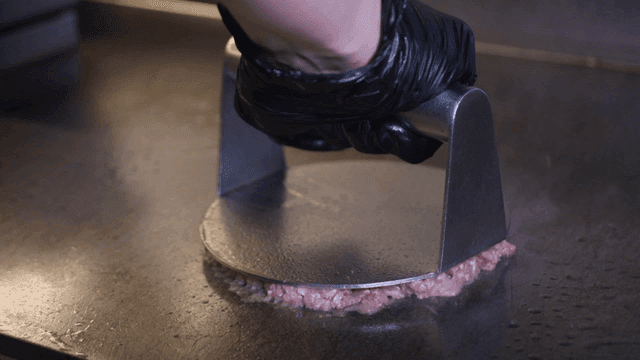 Ground beef patty being pressed on a hot grill