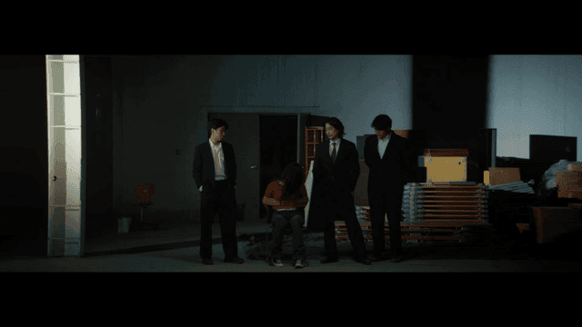 어두운 실내에서 구속된 사람을 둘러싼 정장 차림의 남성들