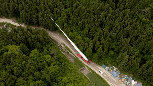 울창한 숲 속 도로에서 풍력 터빈 자재를 운반하는 모습