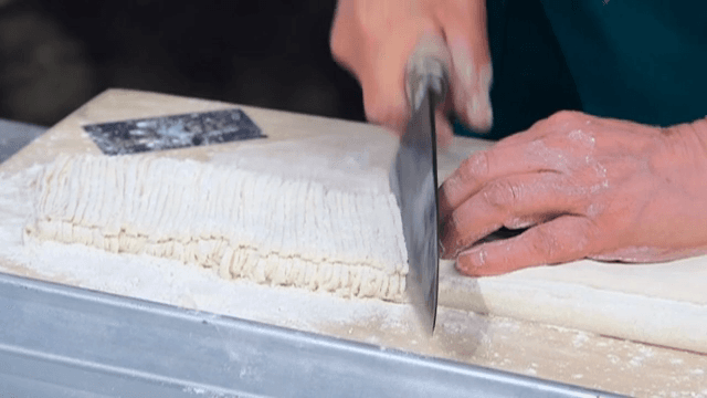 Hands quickly cutting dough on a wooden board