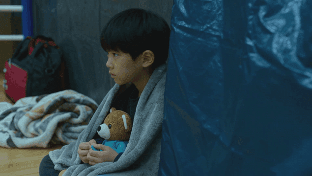 파란 천막 대피소에서 담요에 싸여 곰인형을 안고 있는 아이