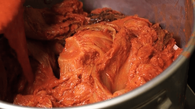 Kimchi broth being poured over kimchi in large pot