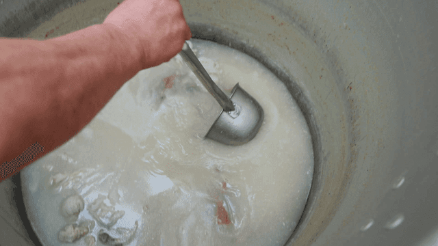 Ladle scooping white bone broth from large pot