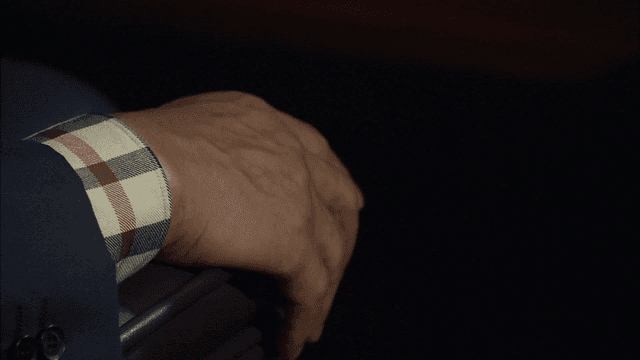 Old man resting his hands on chair in dark room.