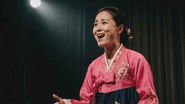 Woman in Hanbok singing passionately on stage