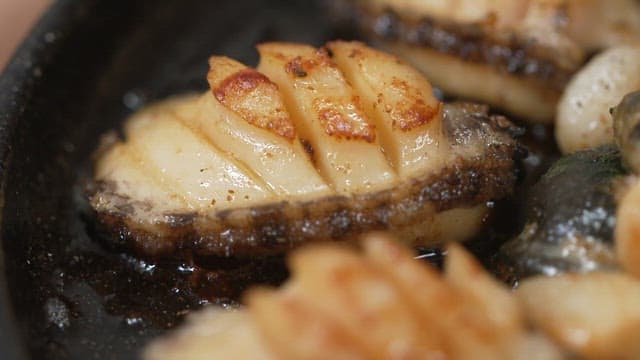 Close-up of grilled abalone sizzling in a pan