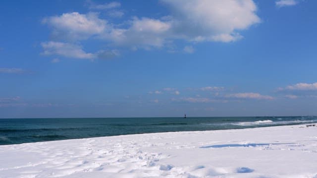 Winter beach scene with snow-covered sand and a clear blue sky