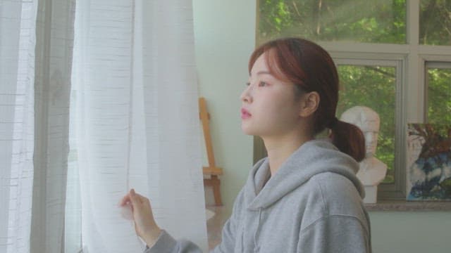 조각상과 그림이 있는 미술실에서 창밖을 내다보는 학생