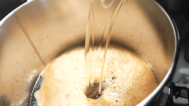 Scene in kitchen where seasoning liquid is poured into large pot.