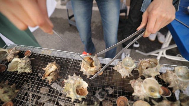 Person holding a deliciously grilled conch on a grill