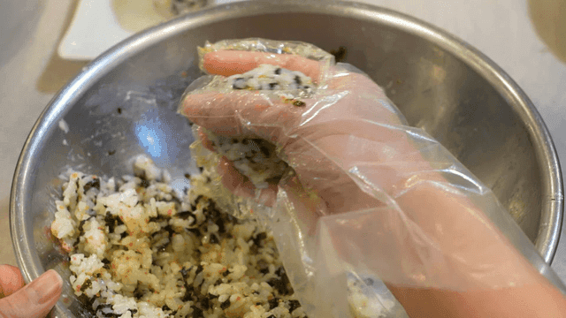 Rice balls made by rolling them into round shape in bowl while wearing plastic gloves