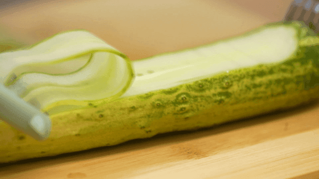 Peeler slicing cucumber on wooden cutting board