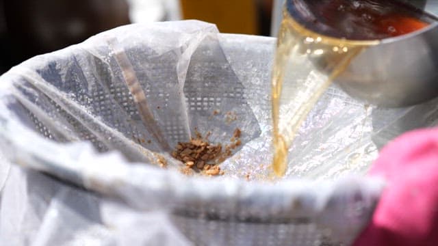 Pouring soy sauce into a sieve for filtering under sunlight