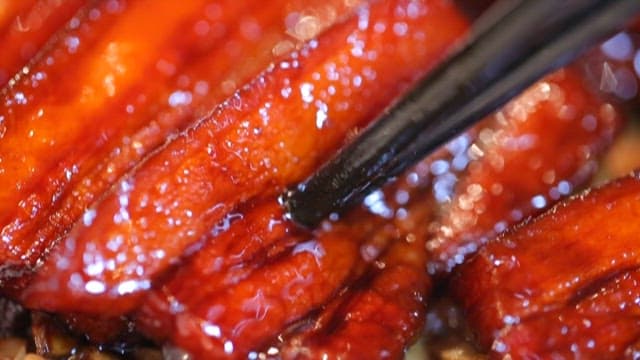 Cutting red braised pork belly with chopsticks