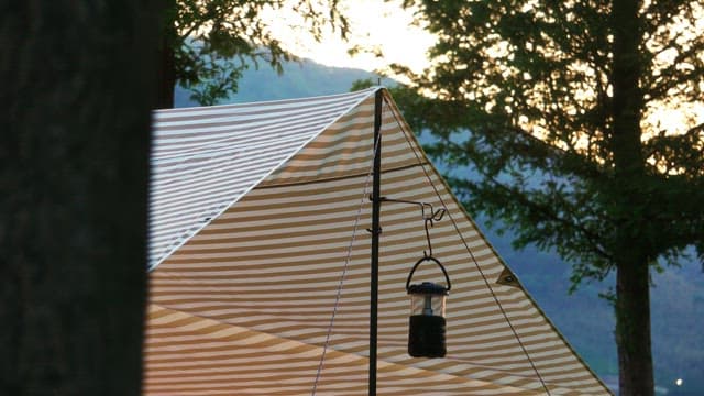 Lantern under a striped tent in the forest during sunset