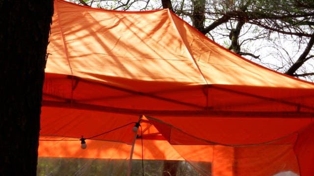 Person erecting an orange tent under the sunlight